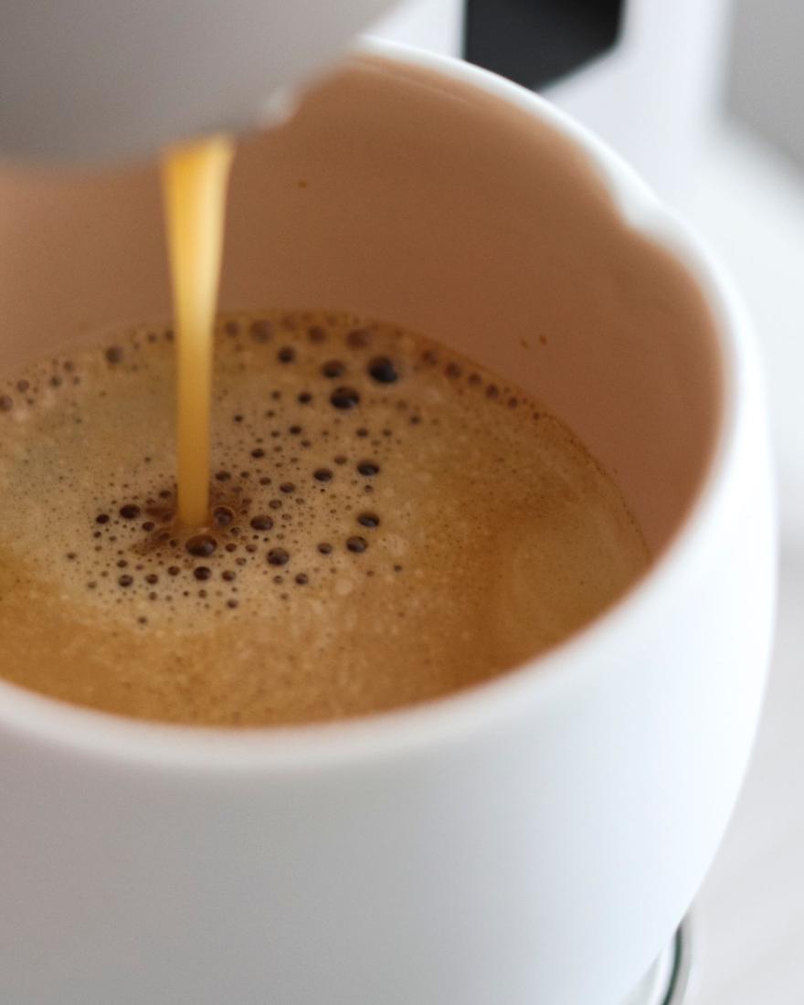 Close-up of espresso pouring from a capsule machine into a white cup, crema forming